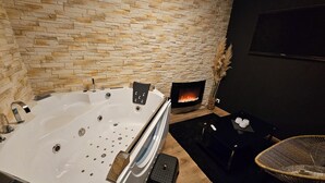 Un baño moderno con pared de piedra, una bañera independiente, chimenea y una silla de mimbre.