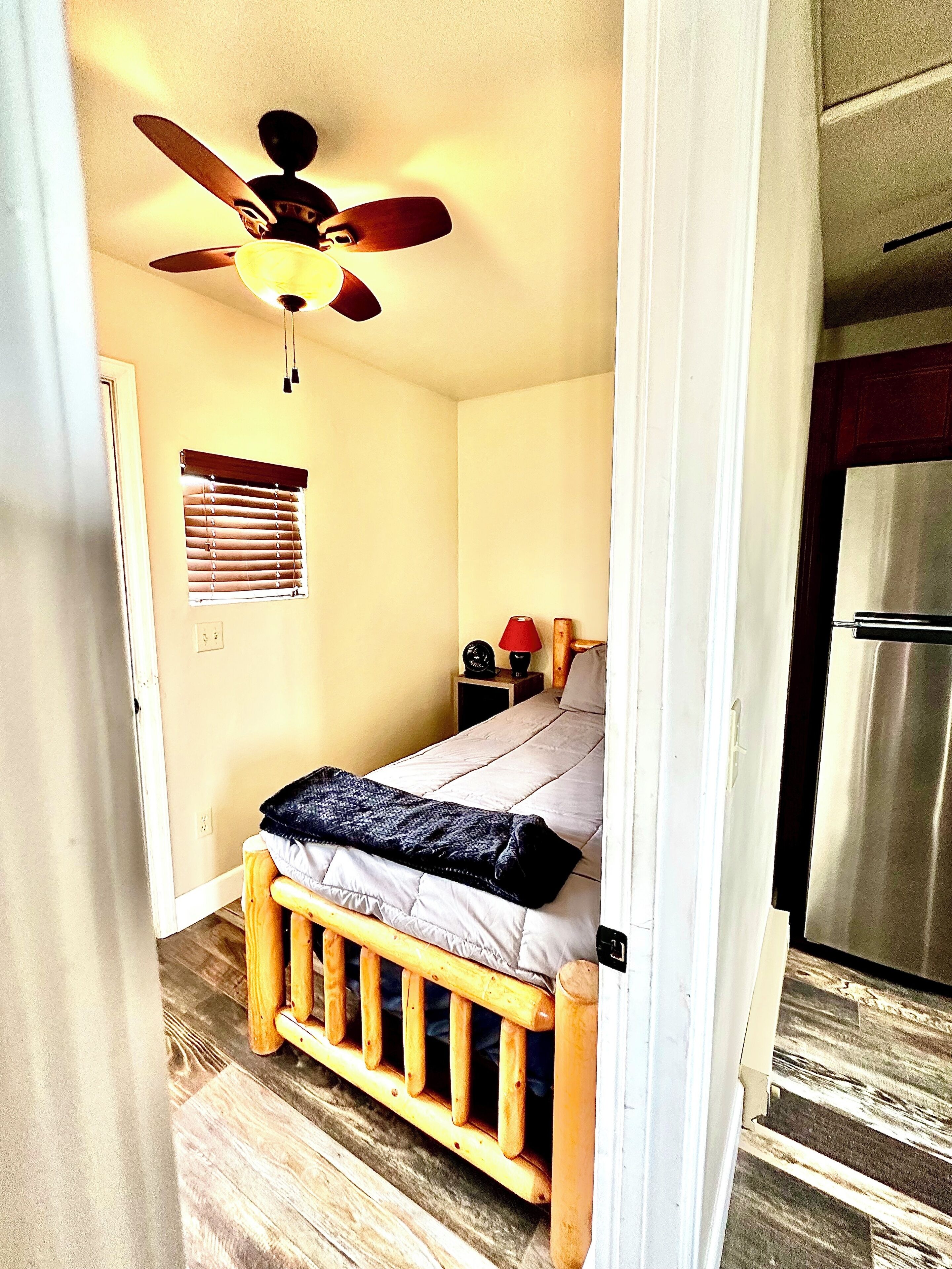 A bedroom with a bed, a ceiling fan, a nightstand, and a window with blinds.