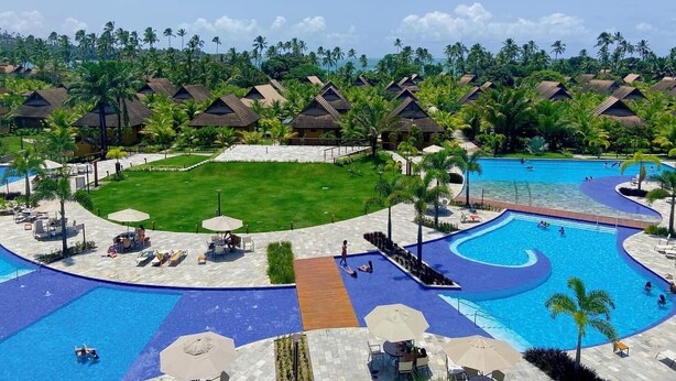 Un resort con varias cabañas, una piscina central y vegetación circundante.