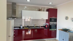A modern kitchen with red cabinets, stainless steel appliances, and a tiled backsplash. - Esperamos por si nas Suas Próximas Férias (Folhadal, Viseu, Portugal)