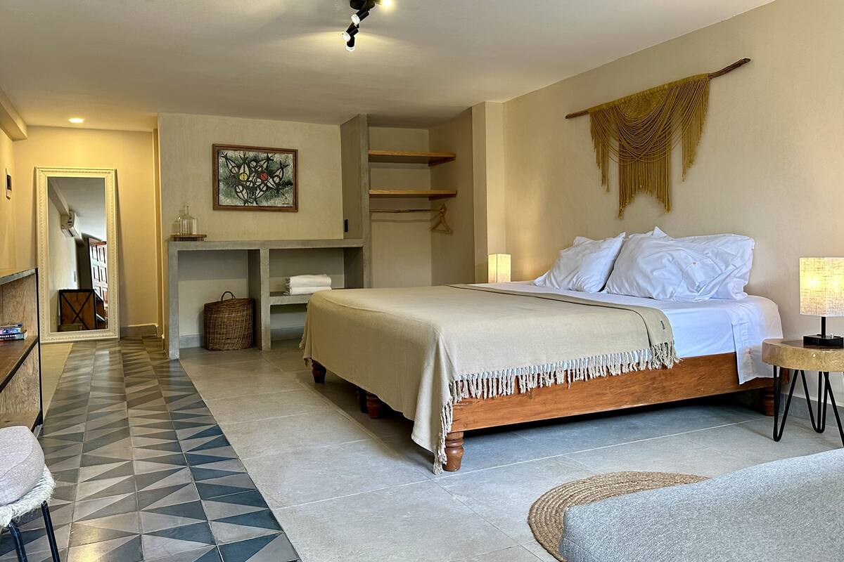 A bedroom with a bed, bedside table, lamp, and a hanging macrame wall decoration.