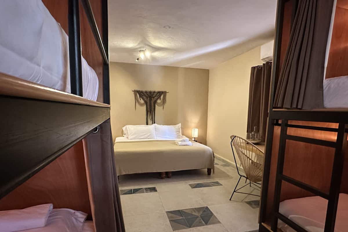 A hotel room with bunk beds, a single bed, a chair, and a small table.