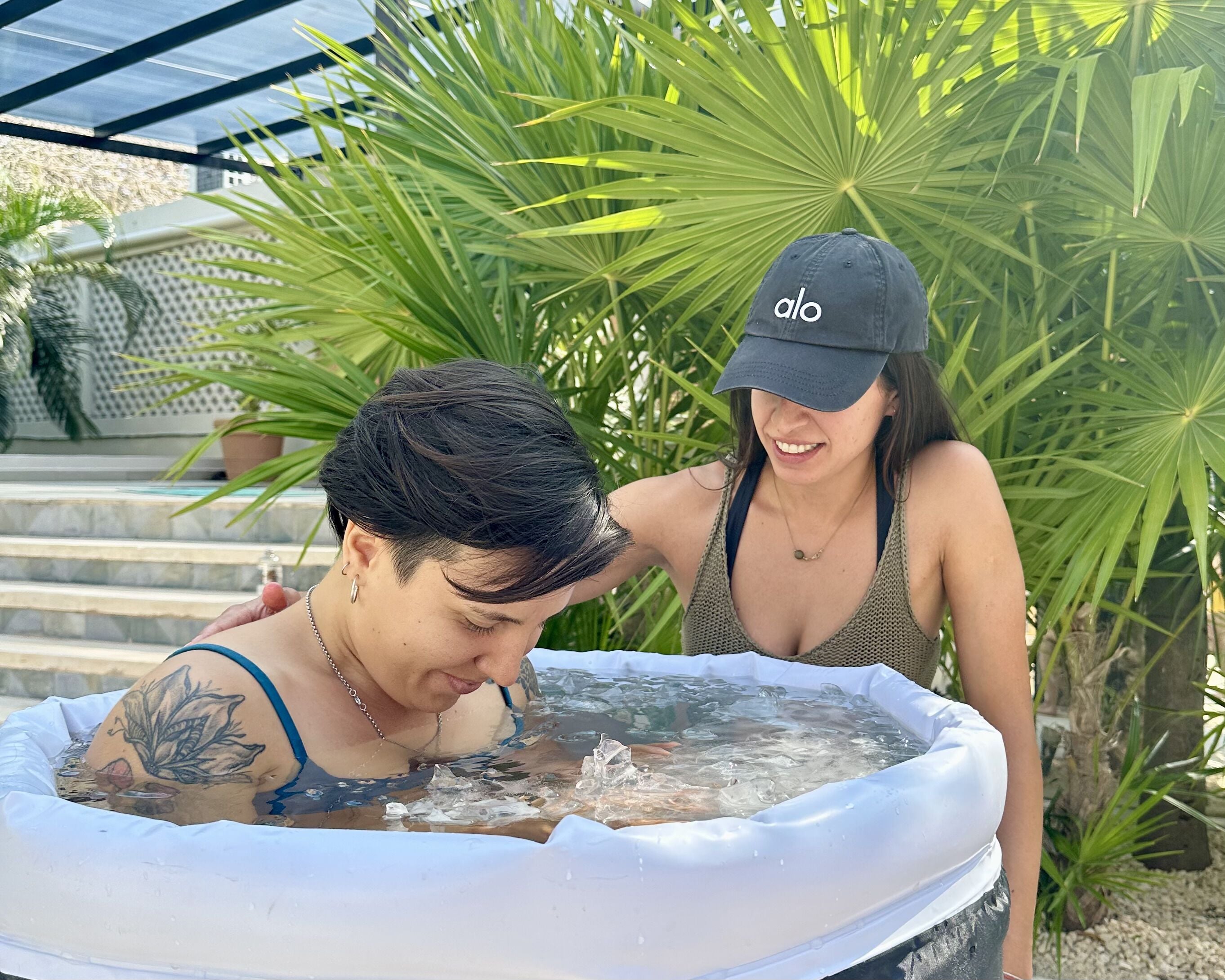Two people in a hot tub with a tropical background.