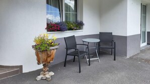 A small outdoor seating area with two chairs and a table, a window with flower boxes, and a decorative wooden planter. - Christians Hamat by Interhome (Ischgl)