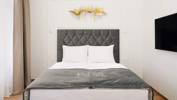 Een netjes opgemaakt bed met een grijs hoofdbord en witte beddengoed, een aan de muur bevestigde televisie en een decoratief kunstwerk in de vorm van geluidsgolven erboven.