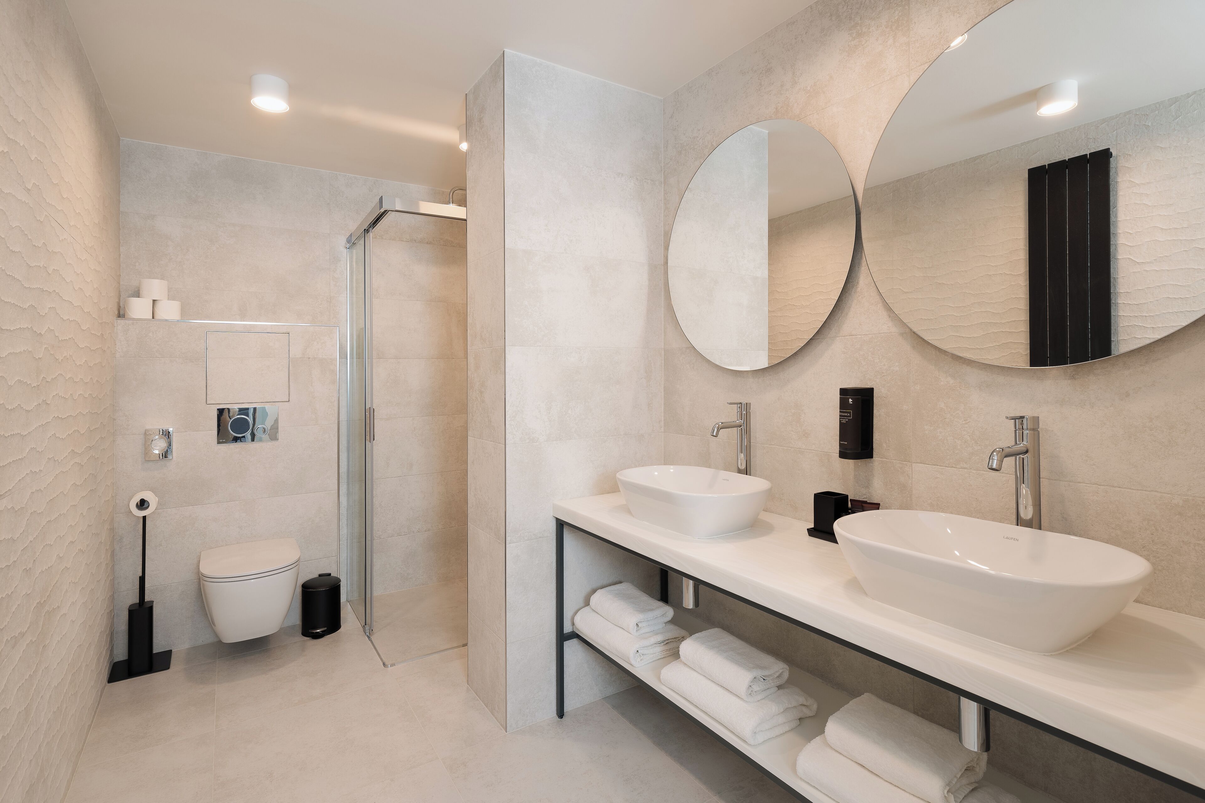 A modern bathroom with a glass shower enclosure, a white sink, and two large mirrors.