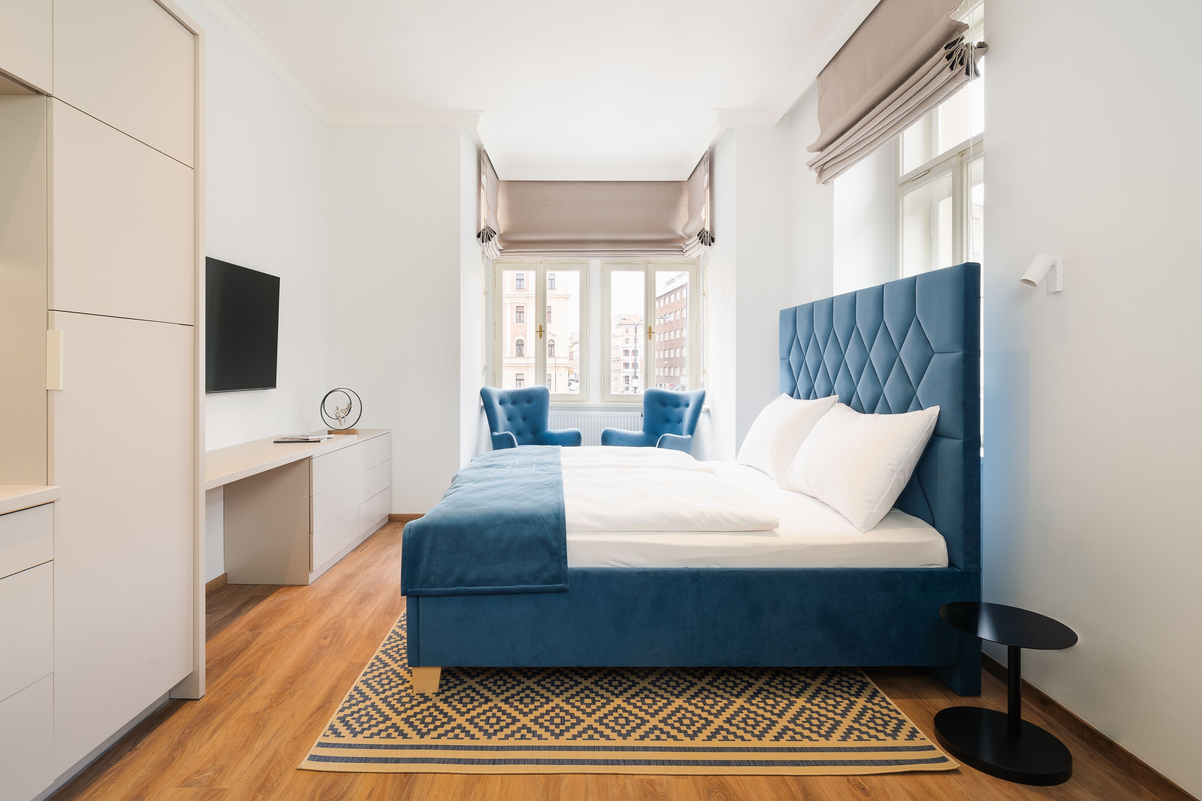 A modern bedroom with a large bed, a desk, and a TV.