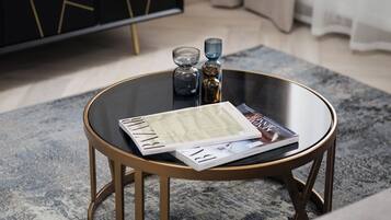 A round glass coffee table with a gold frame, a magazine, and a glass vase on a grey rug.