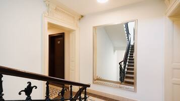 A staircase with a handrail, a large mirror reflecting the stairs, and a door labeled "57" in a hallway with patterned flooring.