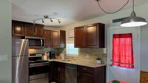 Una cocina compacta con armarios de madera oscura, electrodomésticos de acero inoxidable, encimera de mármol y una cortina roja en la puerta.