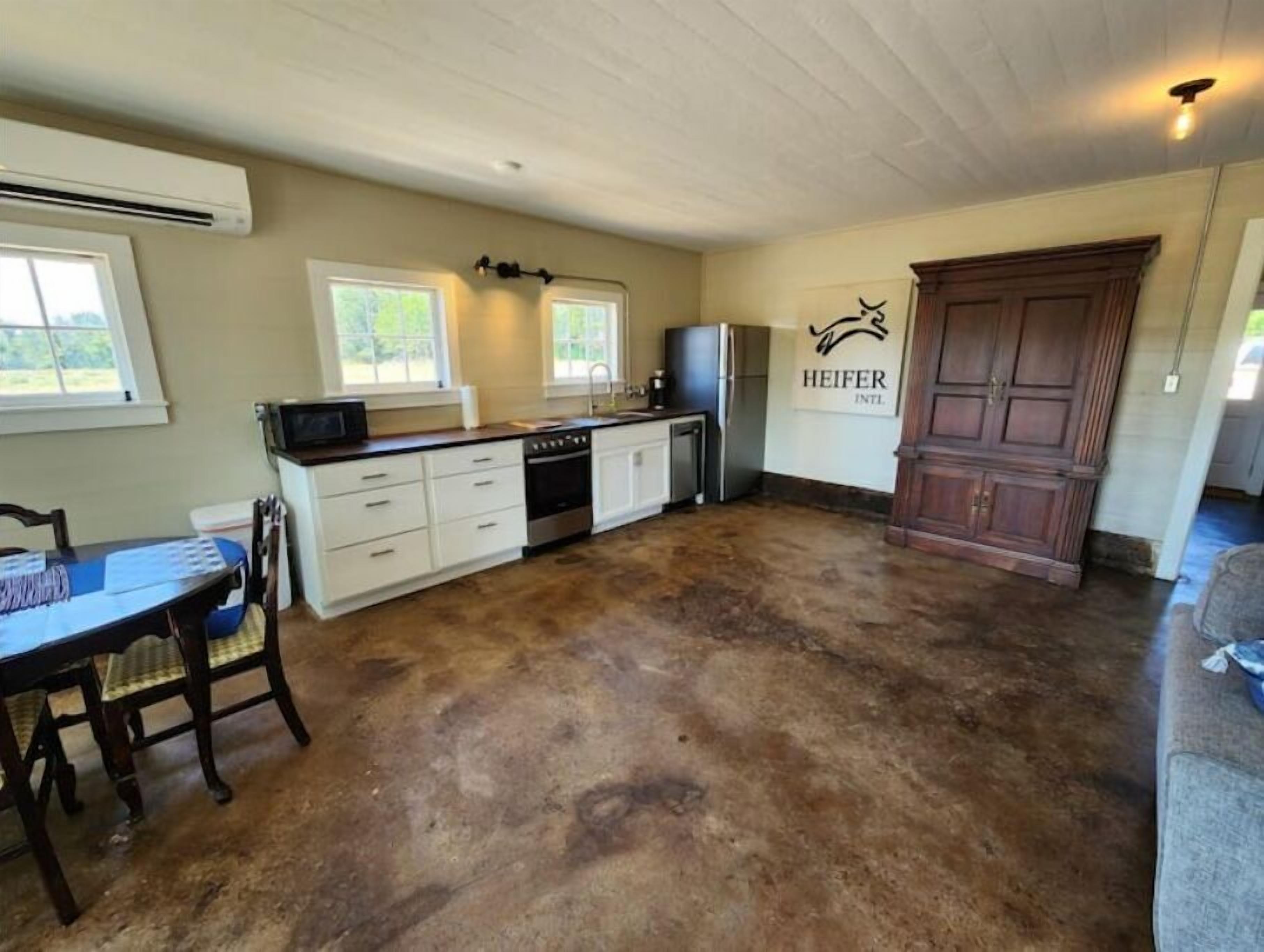 A kitchen with white cabinets, a stove, and a refrigerator. There is a dining table with chairs and a sign on the wall.