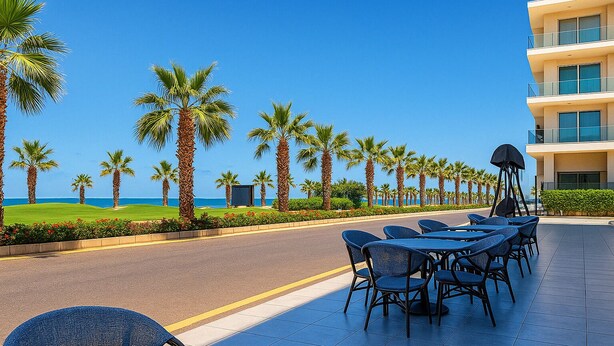 Eine Hotelterrasse am Meer mit Sitzgelegenheiten im Freien, Palmen und Blick auf den Ozean.
