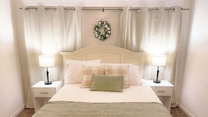Un lit bien fait, recouvert d’une courtepointe matelassée, deux lampes de chevet et une couronne décorative accrochée au mur.