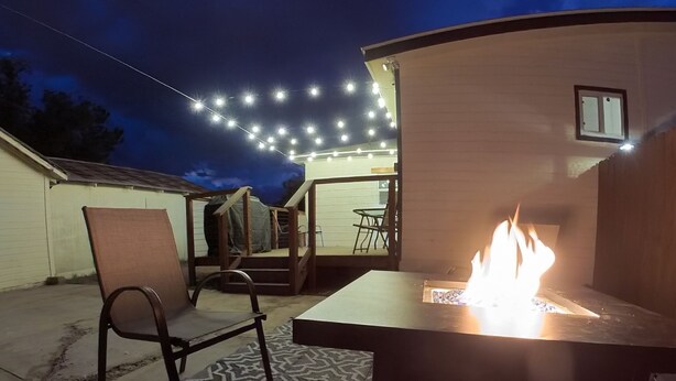 Un espace extérieur aménagé en patio, avec un foyer, des chaises et un tapis à motifs.