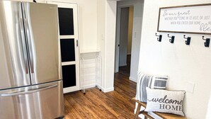 Une cuisine moderne avec un réfrigérateur en acier inoxydable, un meuble blanc et un plancher en bois. Il y a une pancarte sur le mur sur laquelle on peut lire : « Soyez les bienvenus. »