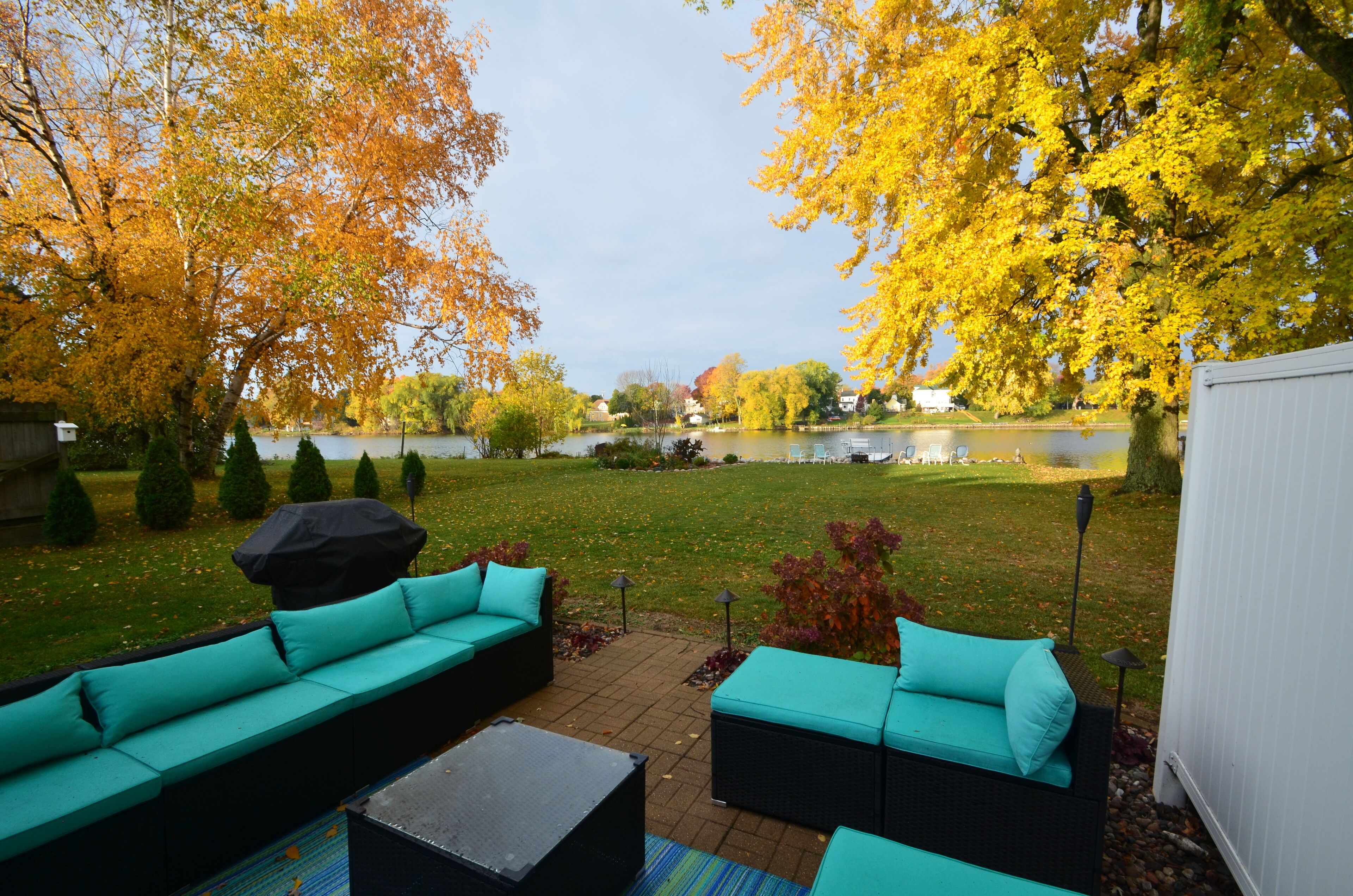 Un patio con mobiliario exterior, vistas a un lago y follaje otoñal.