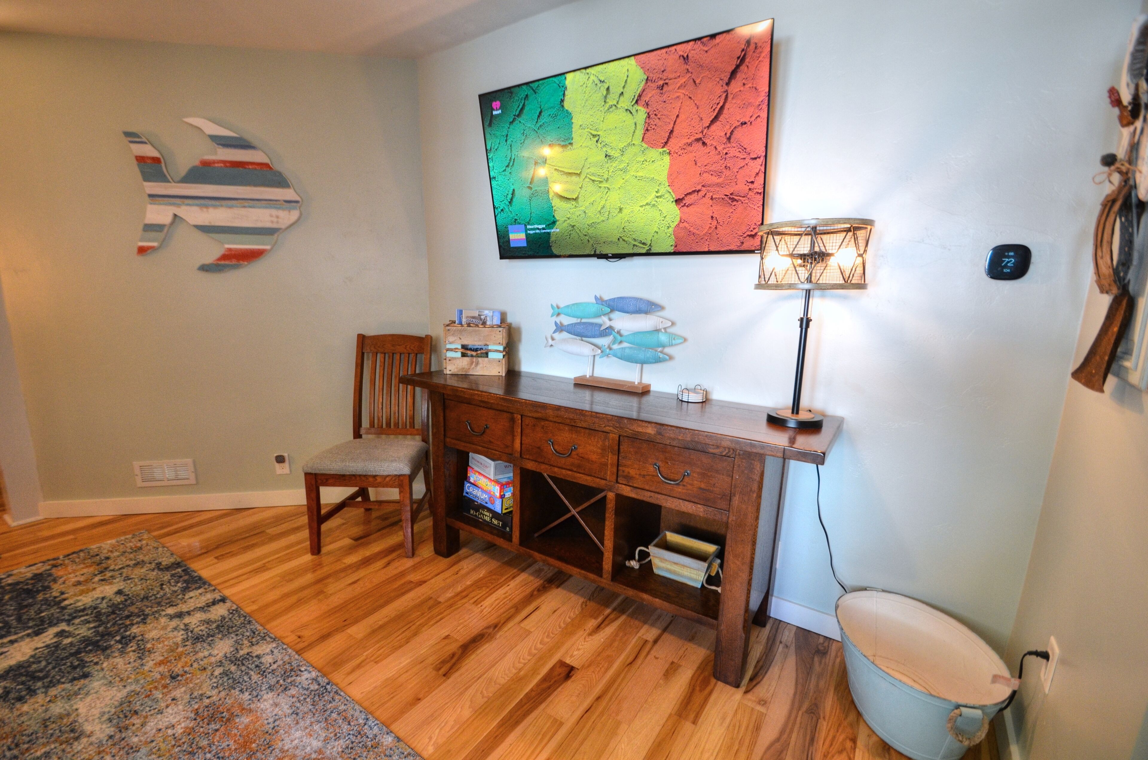 A room with a wooden desk, a chair, a television mounted on the wall, and a lamp.