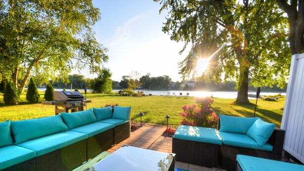 Ett utomhusområde med sittplatser och utsikt över en sjö, omgivet av träd och en grill.