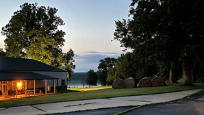 A building with a covered outdoor area, a paved pathway, and hay bales in the background. - A spacious finely-appointed luxury hideaway, nestled in the Ozark Mountains. (Lebanon)