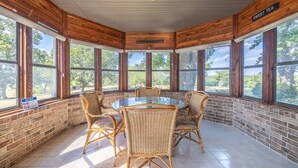 A sunroom with a glass table surrounded by wicker chairs, large windows, and a wooden ceiling. - A spacious finely-appointed luxury hideaway, nestled in the Ozark Mountains. (Lebanon)