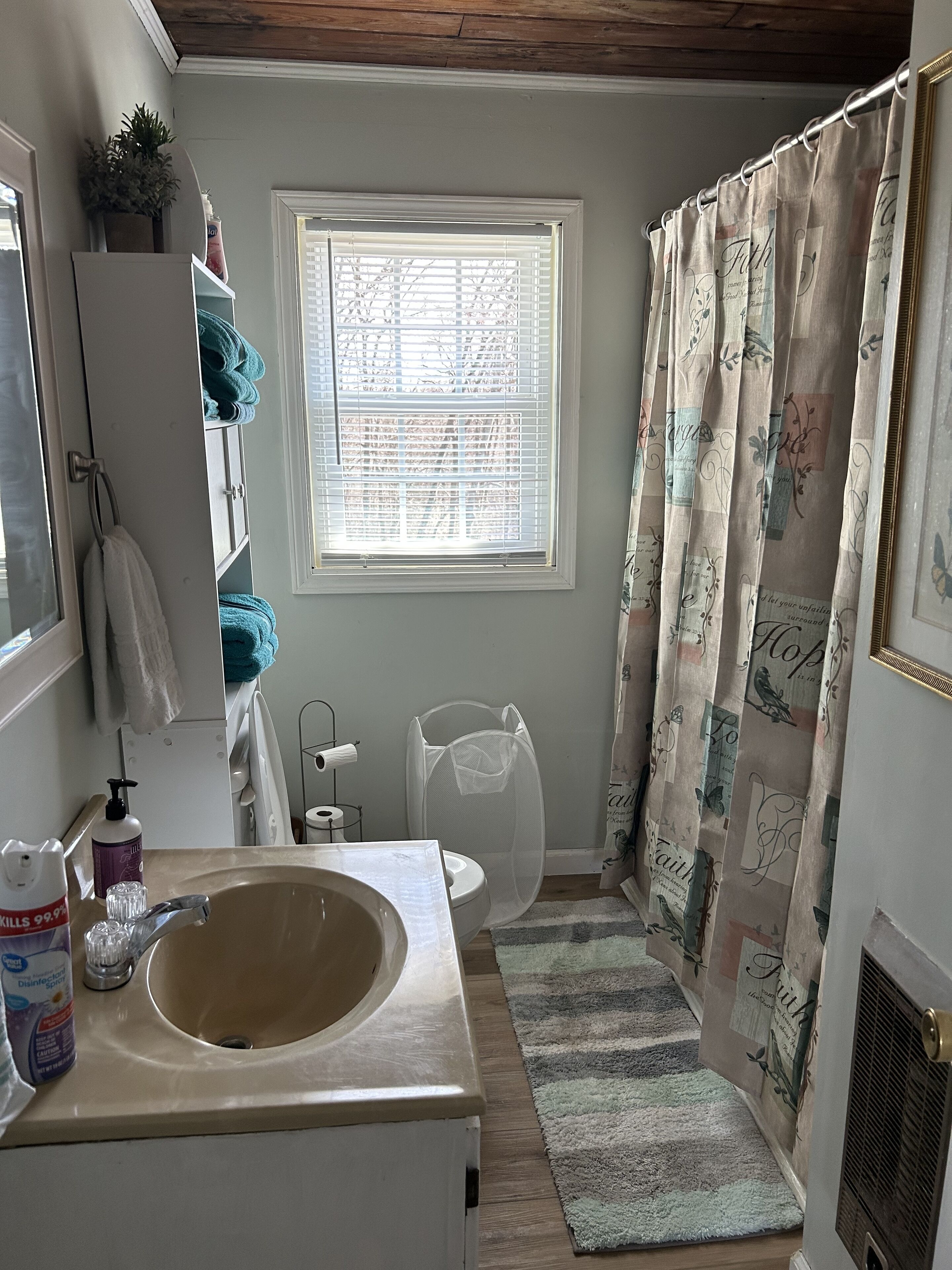 Un bagno con lavandino, wc, finestra e tenda per la doccia.