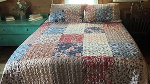 Un dormitorio con colcha acolchada, cómoda verde y ventana con persianas.