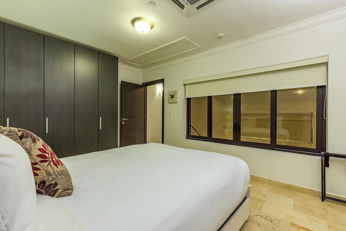 A bedroom with a large bed, dark wooden wardrobe, a window with blinds, and a ceiling light.