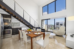 A modern kitchen with stainless steel appliances, a dining area with a wooden table and white chairs, and a staircase leading to an upper level. - Palm Aruba Condos (Noord)