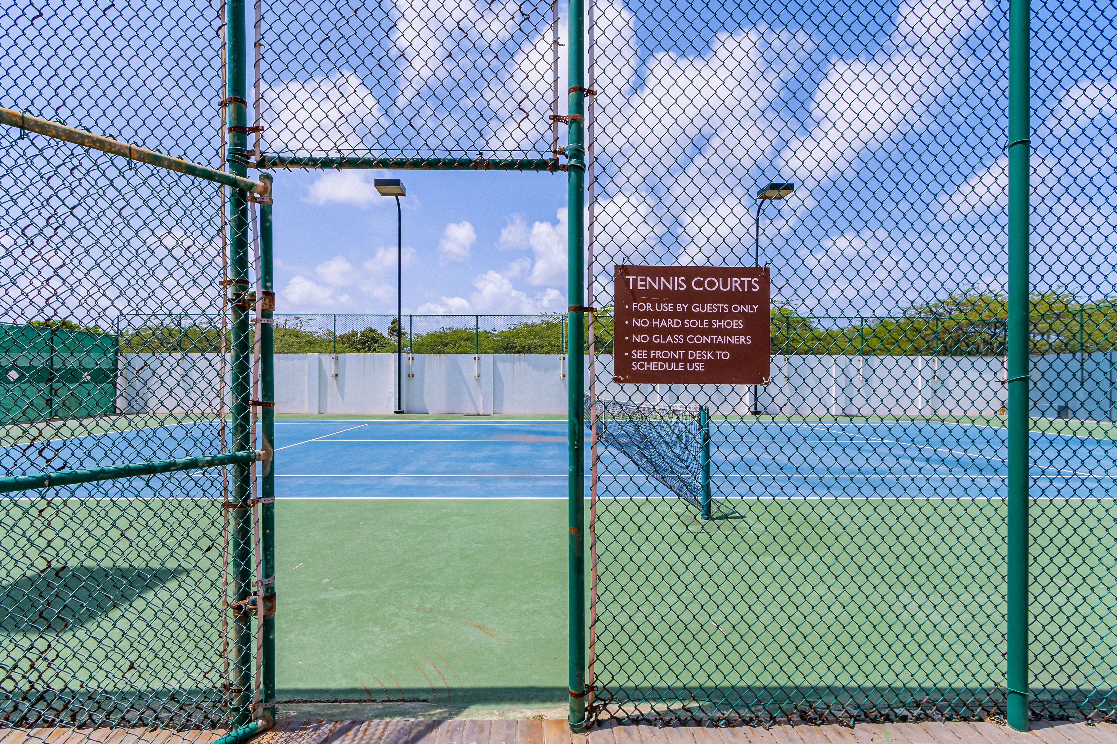 A tennis court with a sign indicating rules and a chain-link fence.
