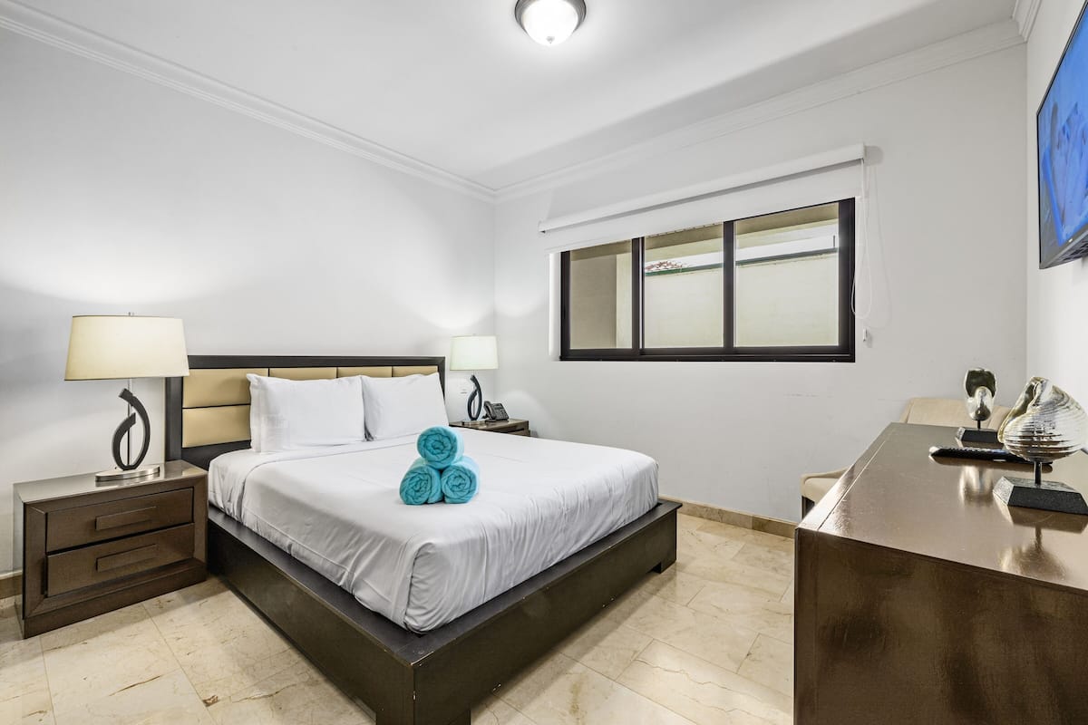 A hotel room with a bed, two bedside tables with lamps, a desk, and a window.
