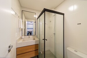 Een moderne badkamer met een douchecabine van glas, een houten wastafelmeubel en een grote spiegel.