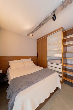 Een slaapkamer met een bed, een houten hoofdbord, een kledingkast met planken en een plafondlamp.