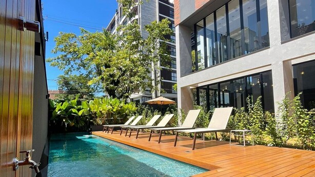 Un bâtiment moderne doté d’un espace piscine, comprenant une terrasse en bois et des chaises longues.