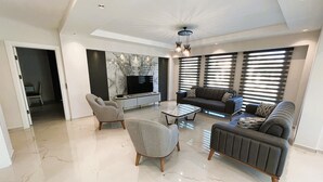 Un salón espacioso con techo alto, televisor de pantalla plana, un conjunto de sofás y una mesa de centro.