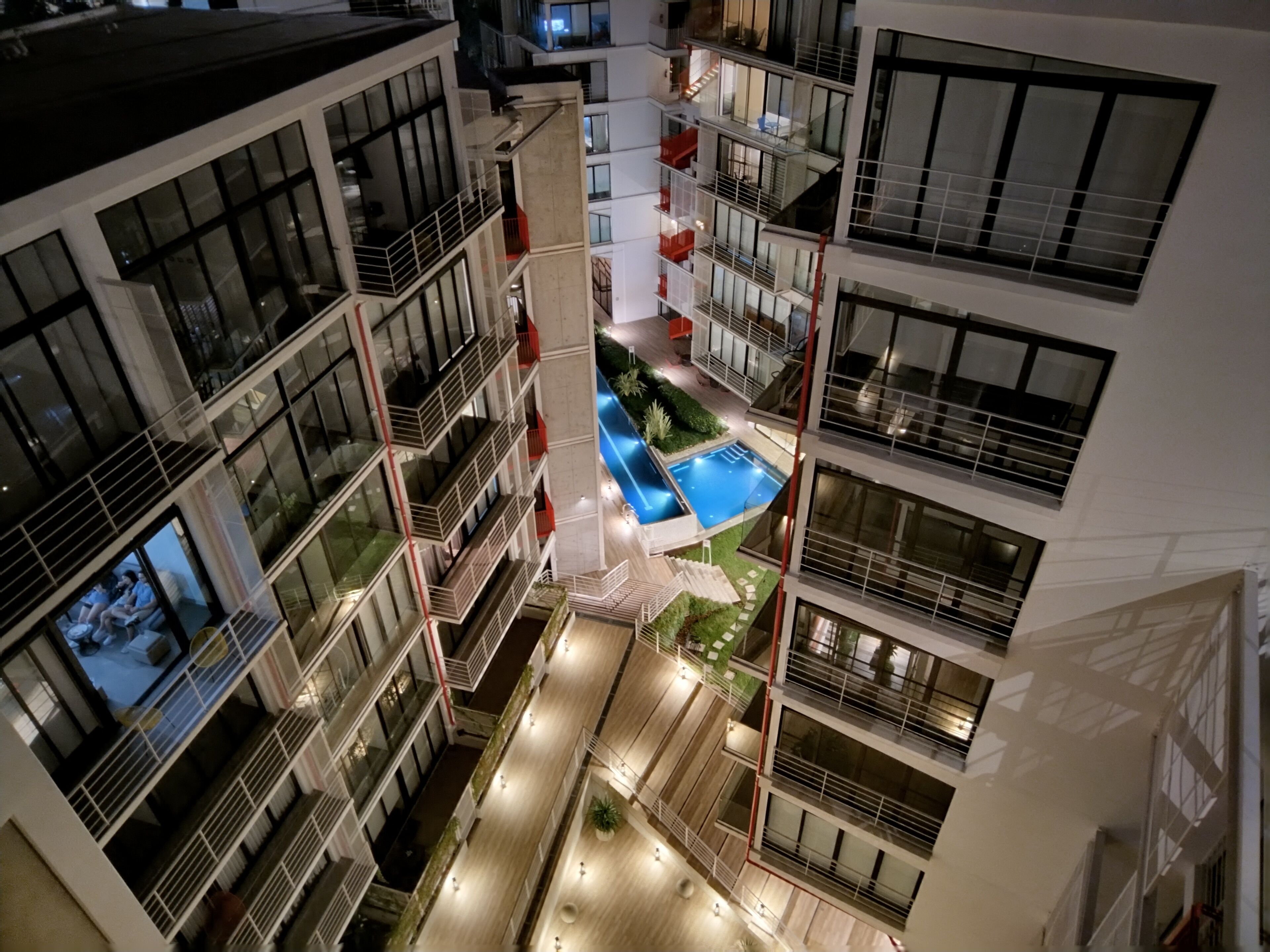 Un edificio de varios pisos con un patio central que cuenta con una piscina, balcones y una escalera.