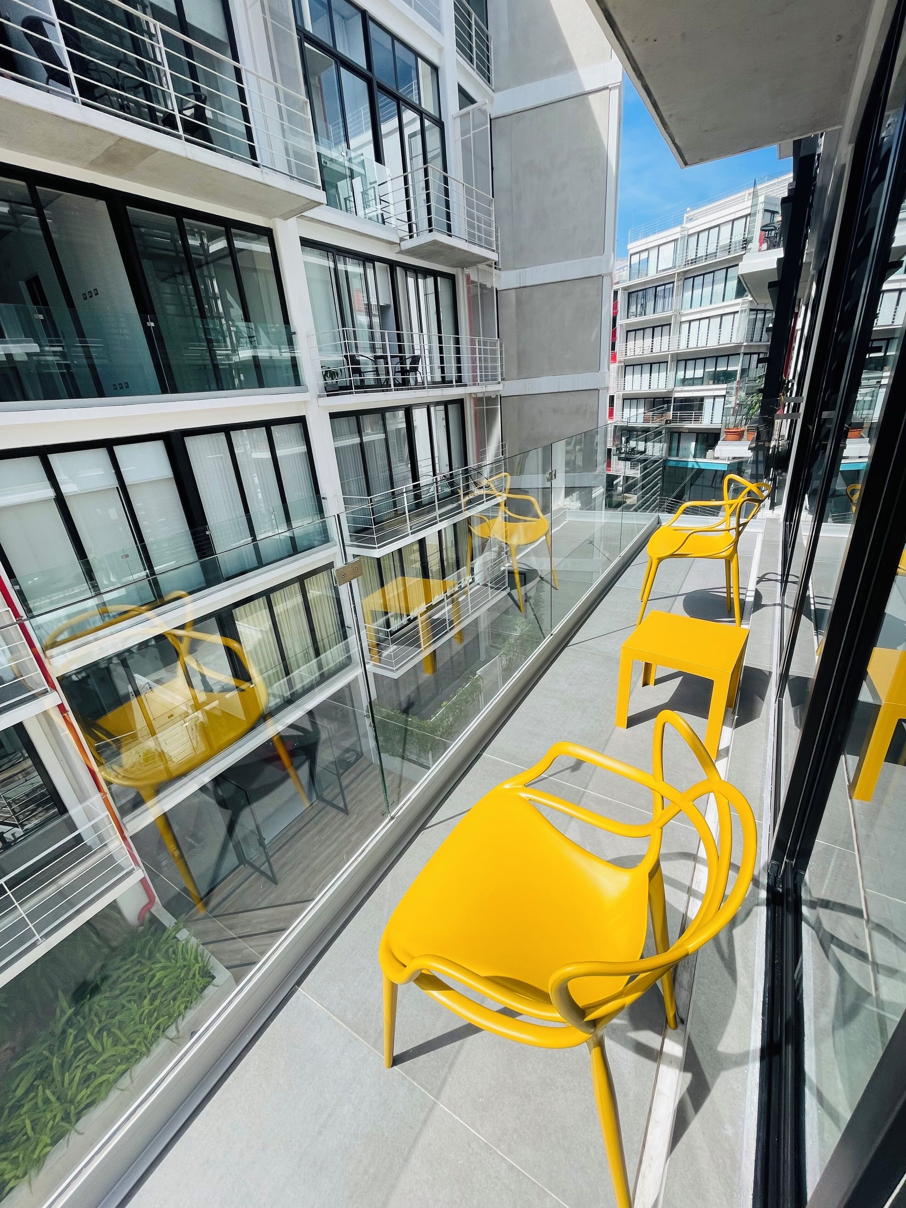 A modern building with multiple floors, large windows, and yellow chairs on a balcony.