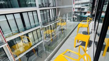 A modern building with multiple floors, large windows, and yellow chairs on a balcony.