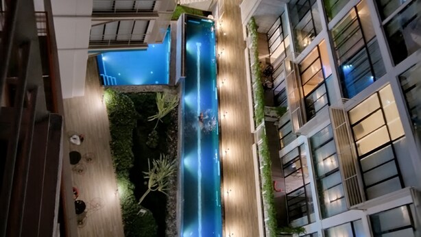 A modern building with a central atrium featuring a blue water feature, surrounded by greenery and illuminated by ambient lighting. - Modern, Cozy Apartment with Air Conditioning Encanto Cayala, Steps from Cayala (Ciudad de Guatemala)