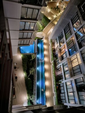 Een modern gebouw met een centraal atrium, inclusief een blauw waterkunstwerk, omringd door groen en verlicht met sfeerverlichting.