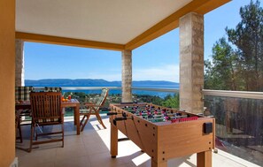 Relax in a serene outdoor space with a view of the water and distant mountains, featuring a foosball table, seating area, and a charming fruit basket.