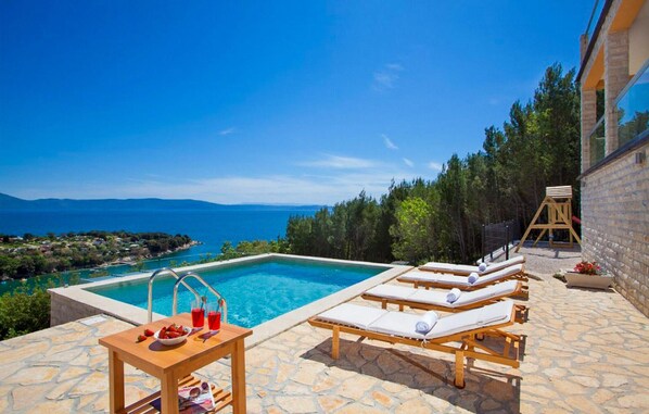 Relax by the serene pool surrounded by lush greenery and a stunning sea view.