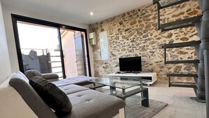 A modern living room with a grey sofa, a glass coffee table, and a stone wall. - Lélégance de la Pierre (Fourques)