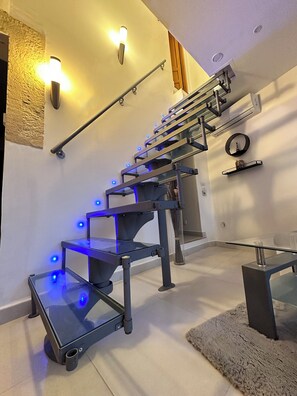 Eine moderne Treppe mit Glasstufen und blauer LED-Beleuchtung, ein runder Spiegel und eine kleine Ablagefläche mit einem dekorativen Gegenstand.