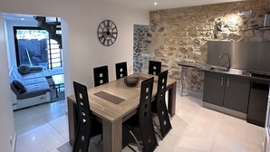 A modern kitchen with a dining area, featuring a stone wall backsplash, stainless steel appliances, and a wooden dining table with black chairs. - Lélégance de la Pierre (Fourques)