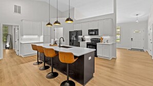 Una cocina moderna con armarios blancos, una isla central con taburetes altos e iluminación colgante.