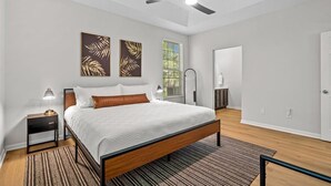 Un dormitorio moderno con una cama, mesitas de noche, un ventilador de techo y obras de arte en las paredes.