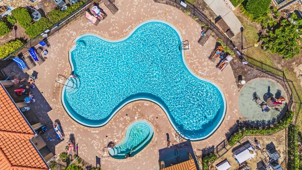 En bild tagen från ovan av en pool med en ovanlig, vågformad design, omgiven av solstolar och solbäddar, samt ett mindre poolområde.
