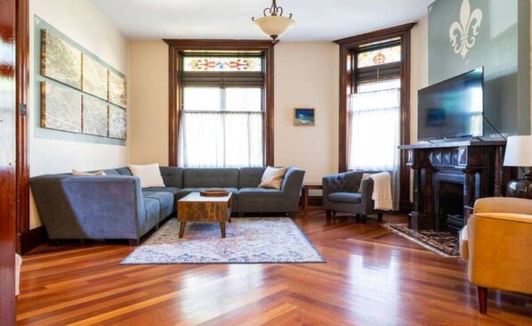 Ein Wohnzimmer mit Ecksofa, einem kleinen Couchtisch, einem Kamin und einem Fernseher.