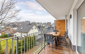 Un balcon avec une table et des chaises en bois, donnant sur un quartier résidentiel avec des maisons et des arbres.