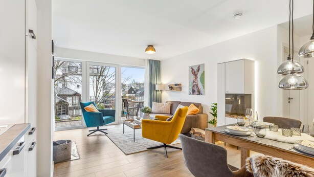 A modern living room with a sofa, armchairs, a dining table, and a view of the outside. - GebirgsResort Winterberg 123 (Winterberg)